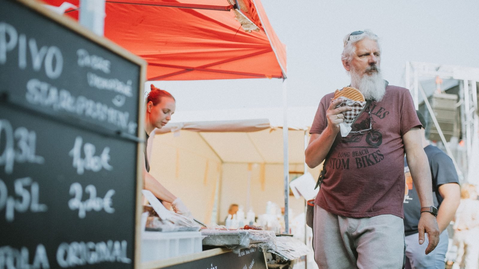Traveler enjoying street food next to a chalkboard displaying menu prices.