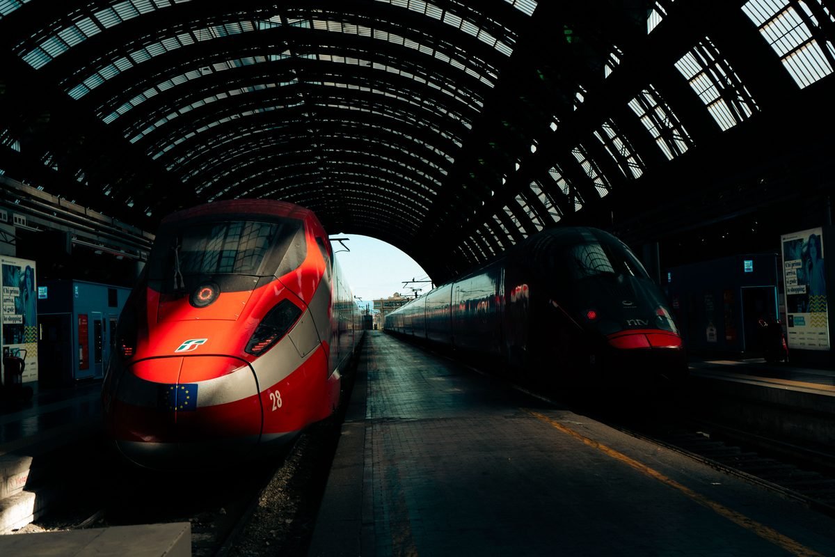 Modern high-speed trains parked under the grand glass roof of Milan Central Station.