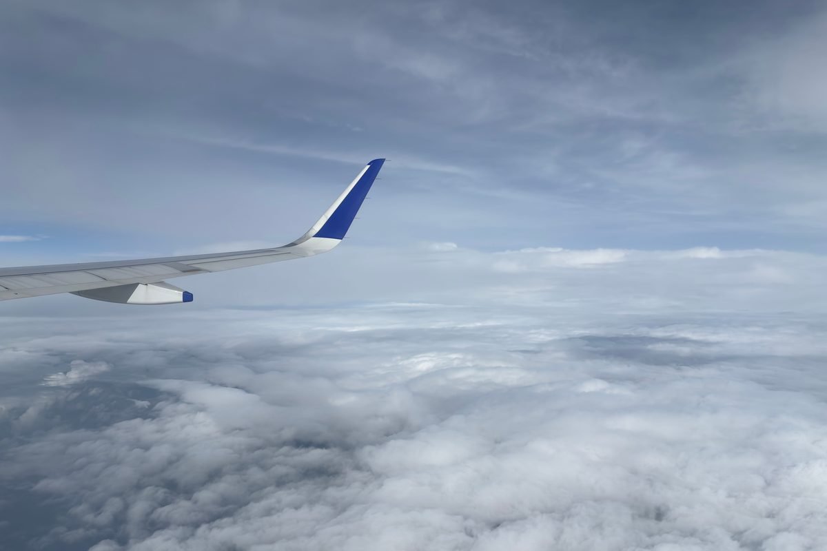 Airplane wingtip soaring above a thick blanket of white clouds in flight.