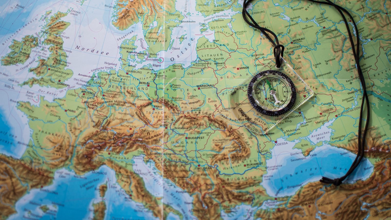 Transparent navigational compass resting on a detailed physical map of Europe.
