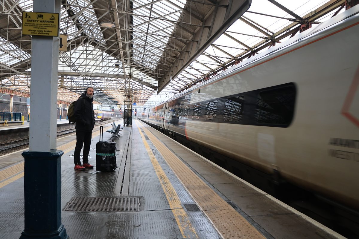 Traveler with luggage waiting on a train station platform as a train arrives.