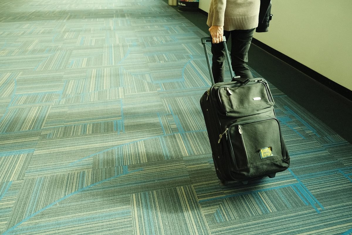 Traveler walking down an airport corridor pulling a rolling suitcase.