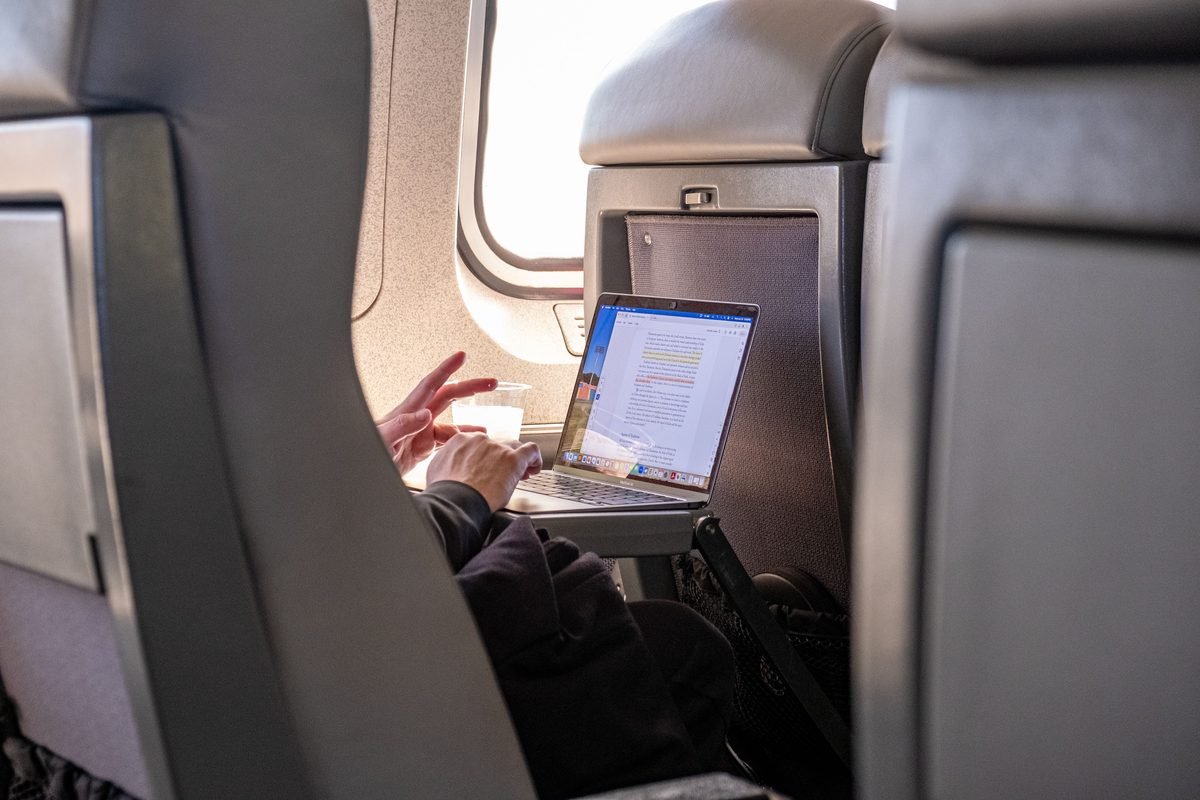 Traveler using a laptop on a tray table inside a passenger train carriage.