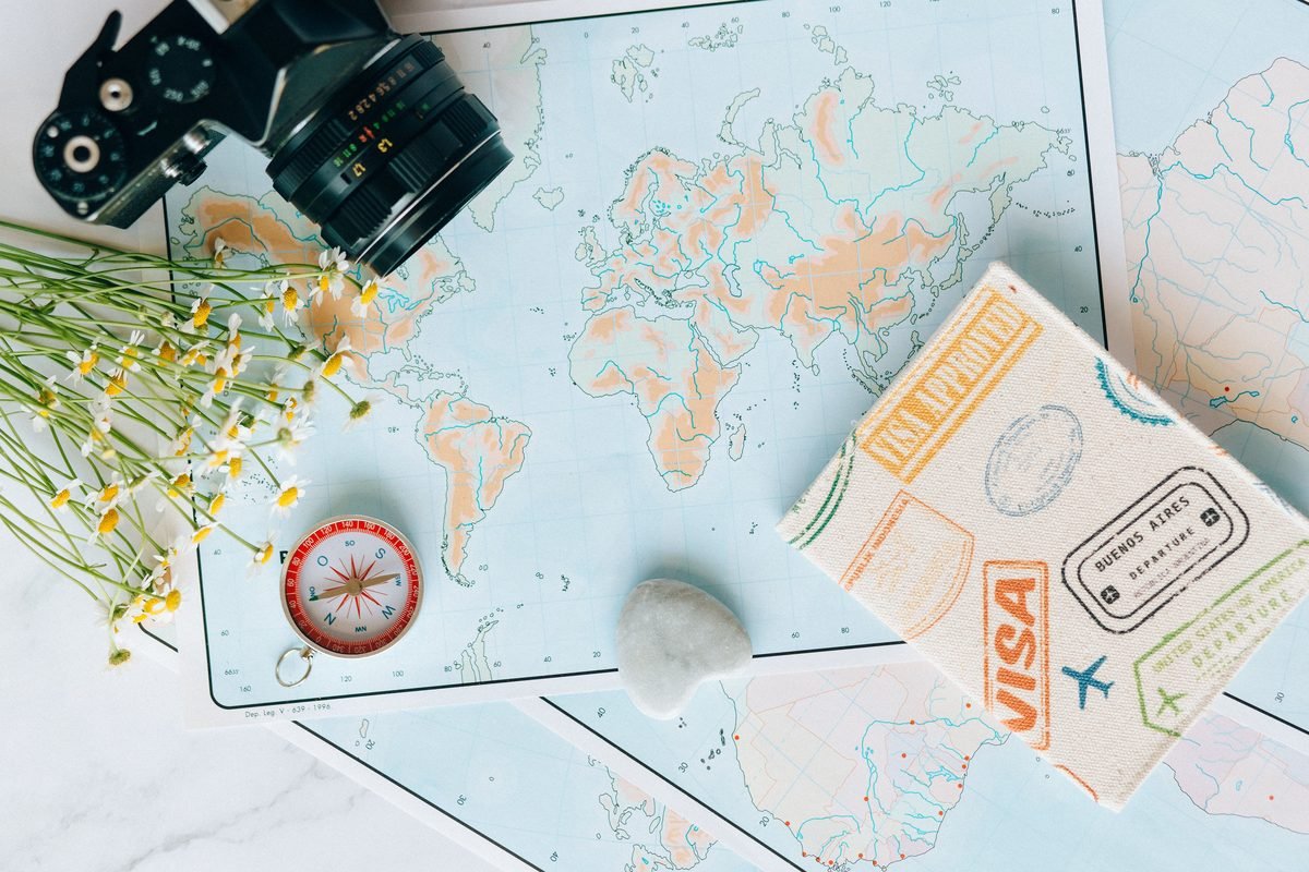 Flat lay of travel essentials featuring a world map, camera, compass, and journal.
