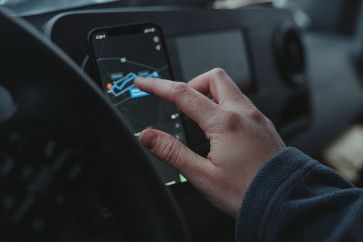 Hand interacting with GPS navigation map on a smartphone inside a vehicle.