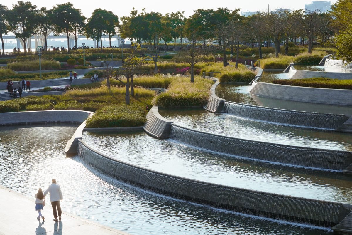Cascading modern water features and walking paths in a landscaped urban park.