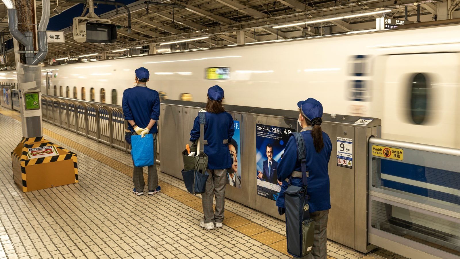 Bullet train speeding through a station with staff on platform
