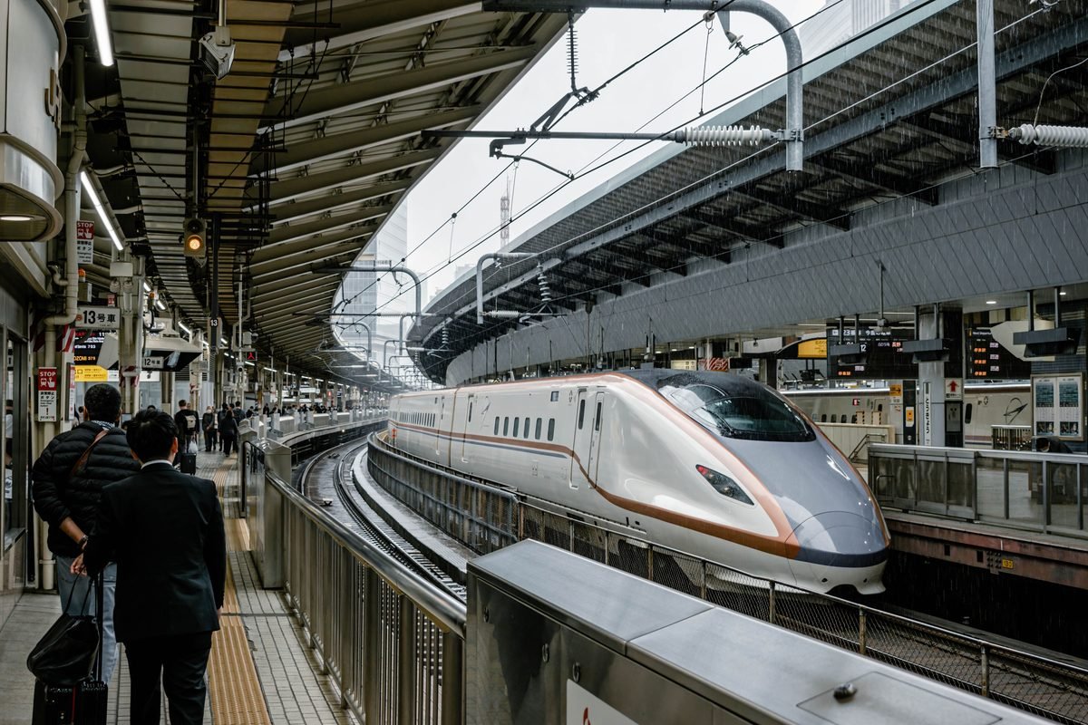 A sleek shinkansen train waits at a Tokyo station platform with passengers nearby
