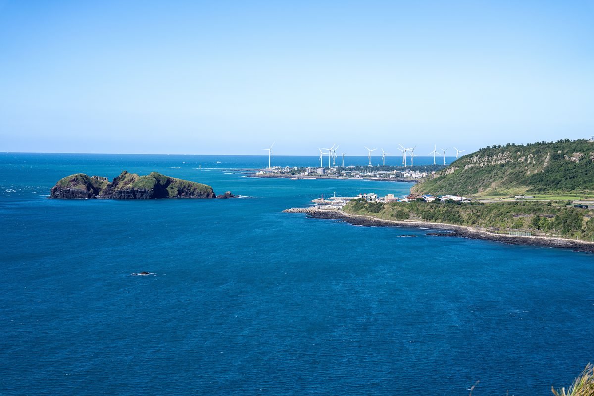 Scenic view of Jeju Island coastline with wind turbines under clear blue skies