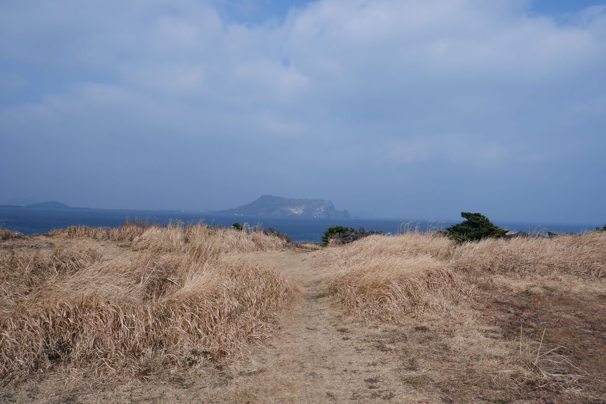 Dirt walking path on the coast of Jeju Island with distant islets