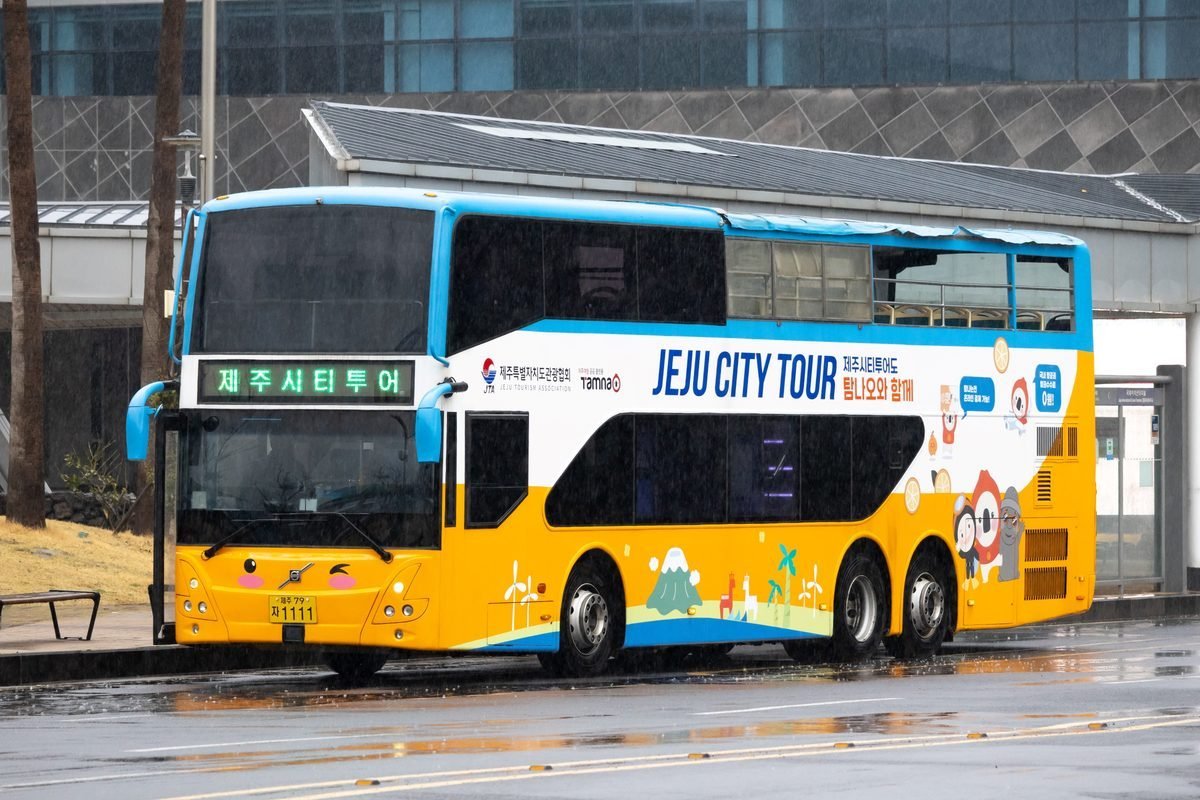 Jeju City Tour double-decker bus waiting at a stop on a rainy day