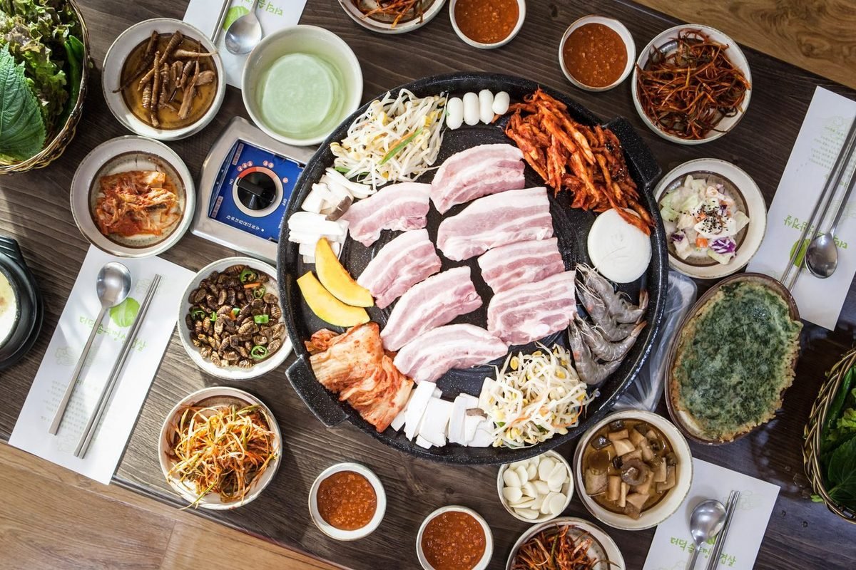 Korean pork belly barbecue table with grill, lettuce, kimchi and side dishes