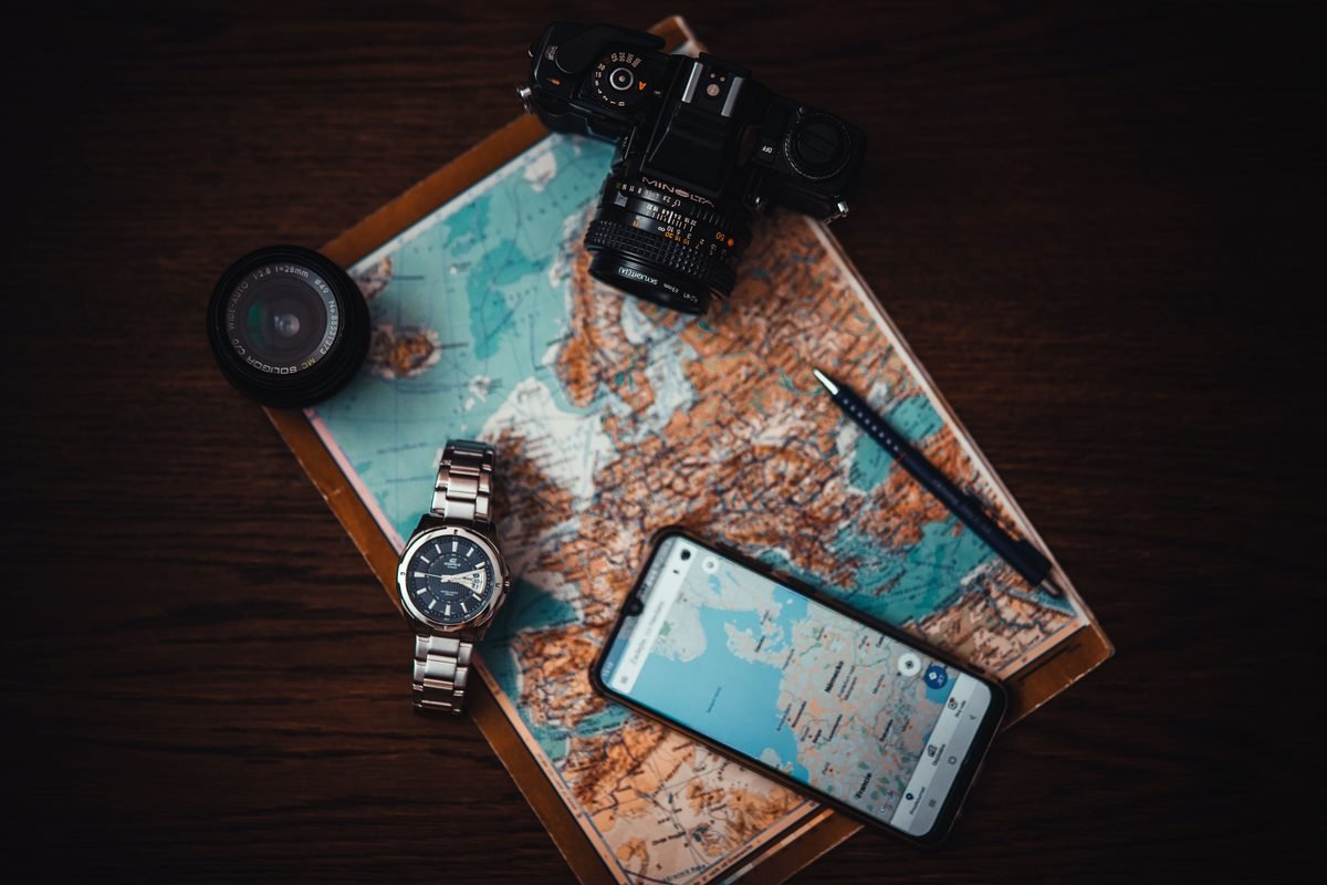 Travel essentials including a map, camera, and smartphone on wood.