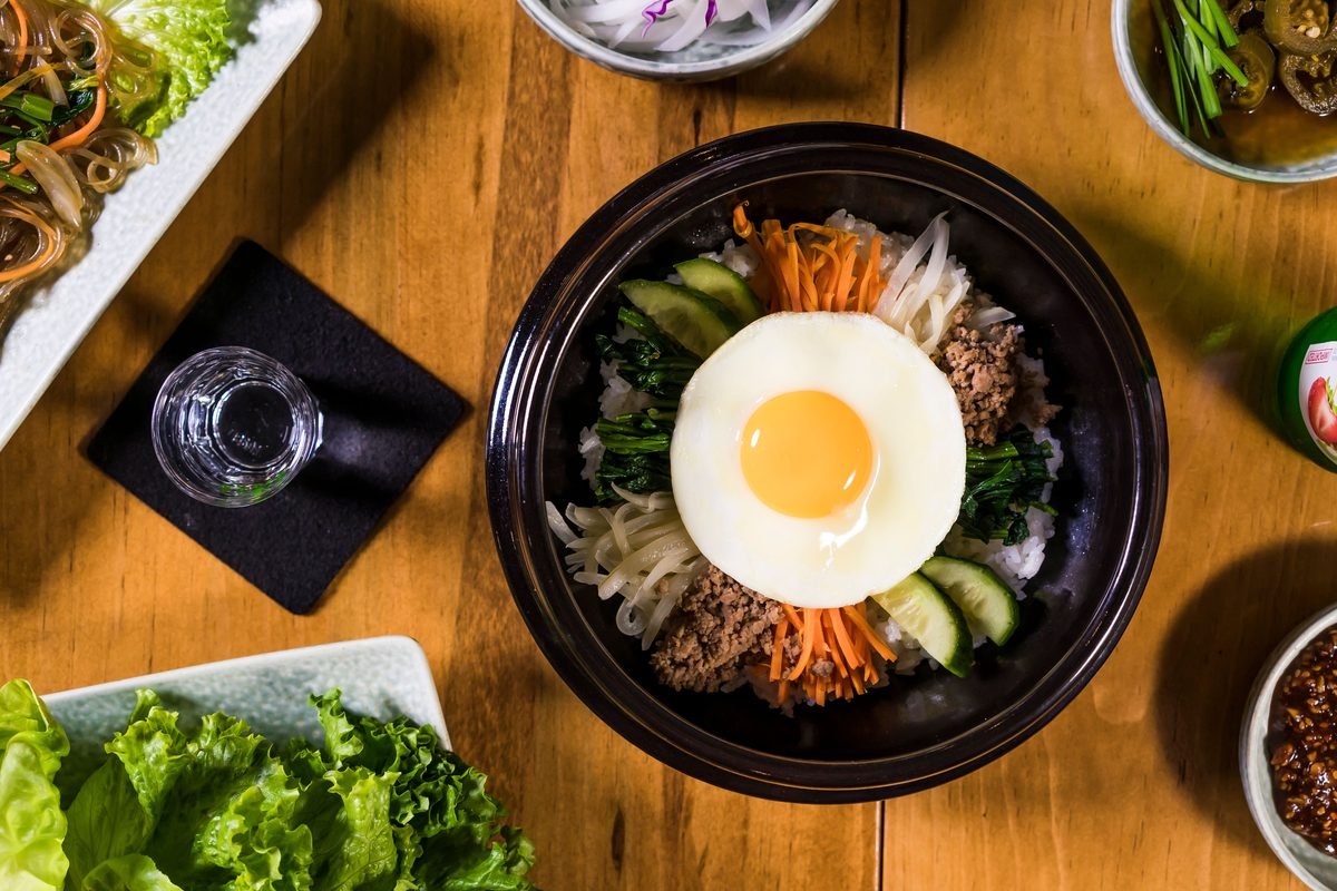Top-down view of a dark ceramic bowl of bibimbap with an egg on top.