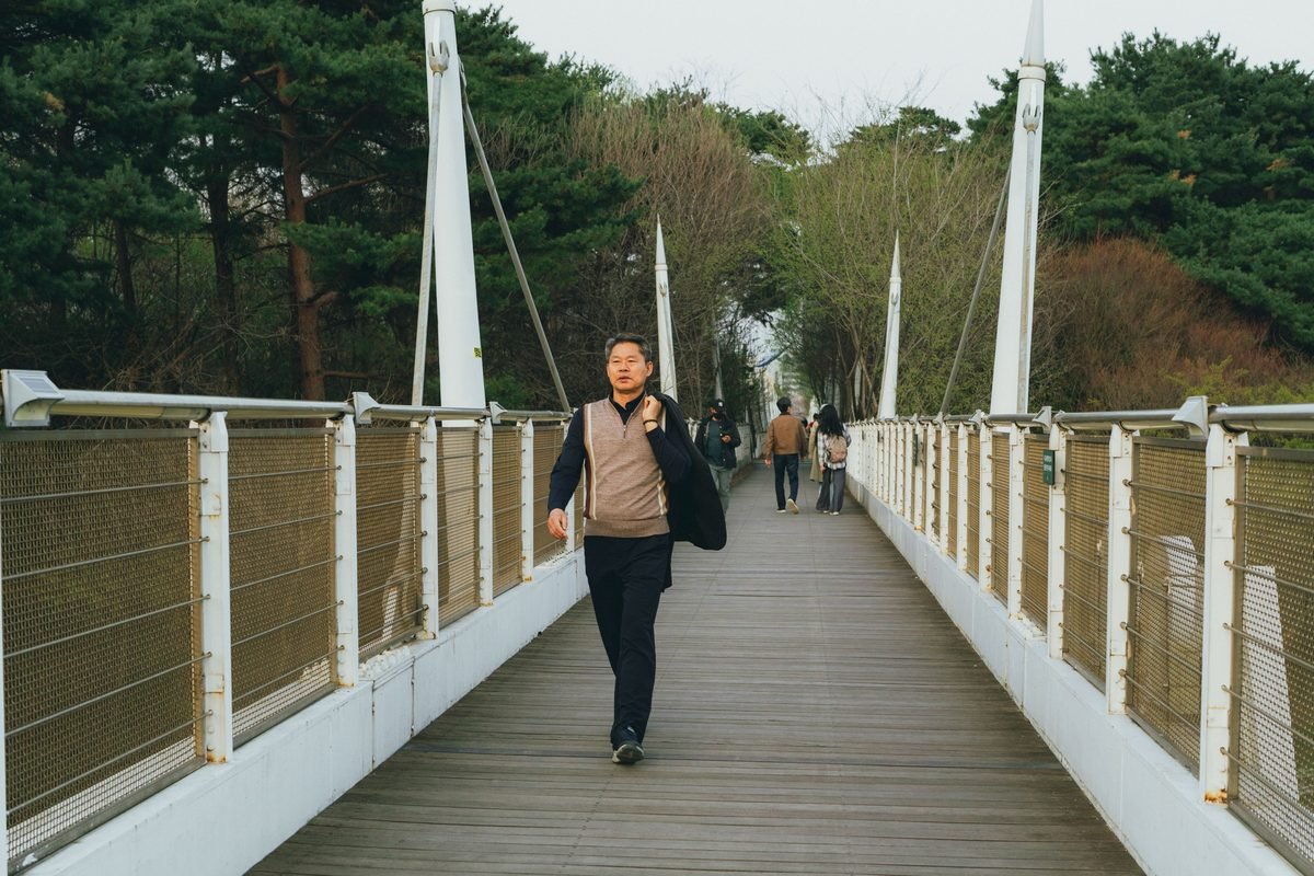 A man walking on a wooden pedestrian bridge over a park stream