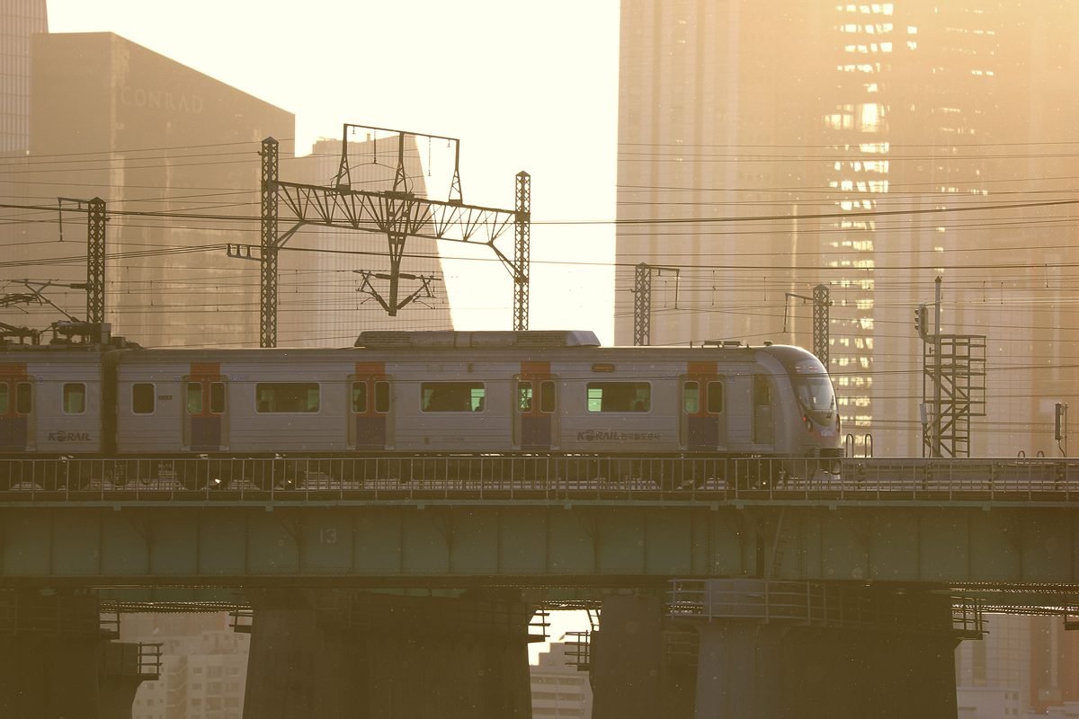 A commuter train crossing a bridge against tall buildings during sunset in Seoul