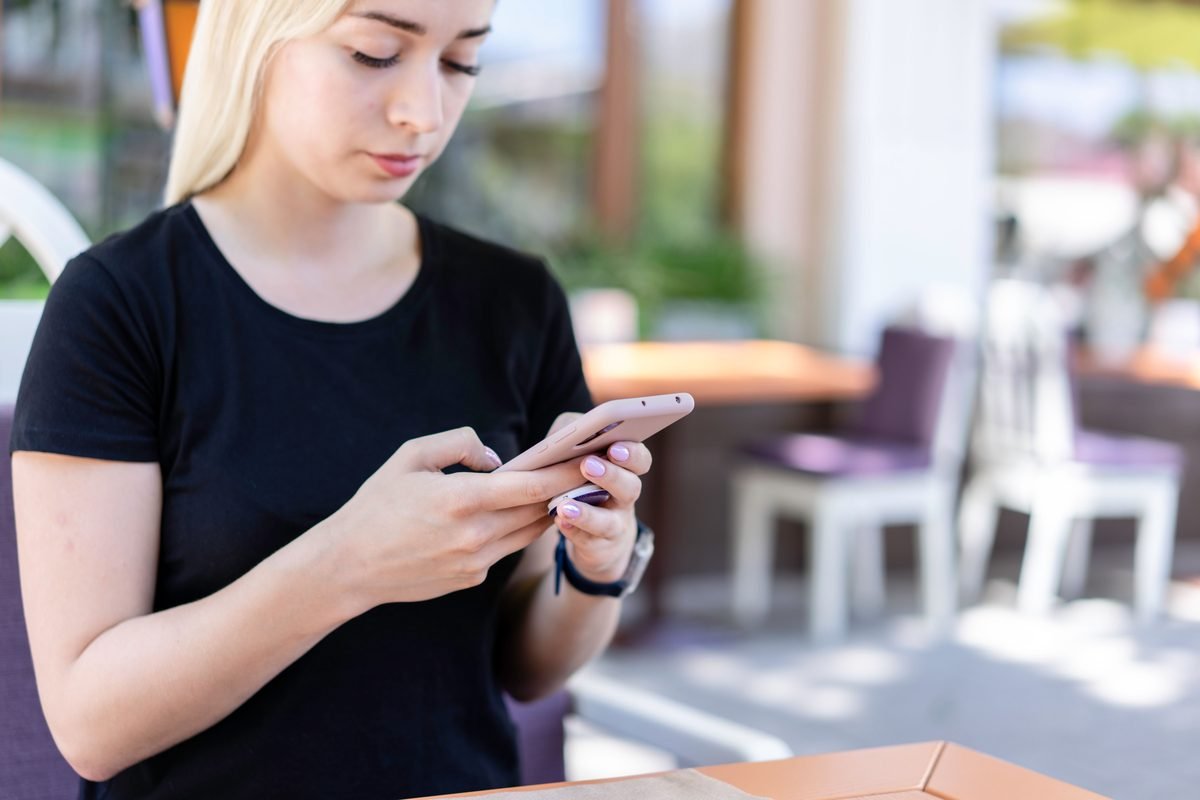 Young woman in a black shirt texting on her smartphone at an outdoor cafe