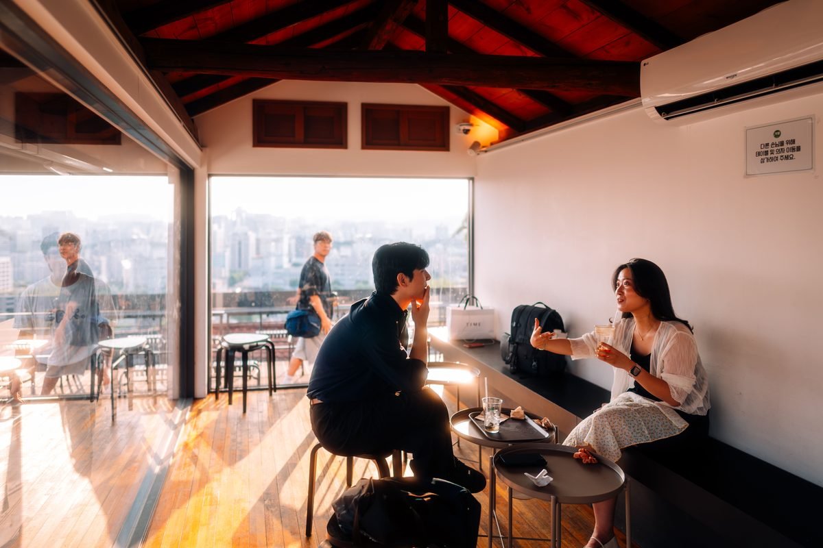 People chatting in a modern Seoul cafe with a city skyline visible through the window.