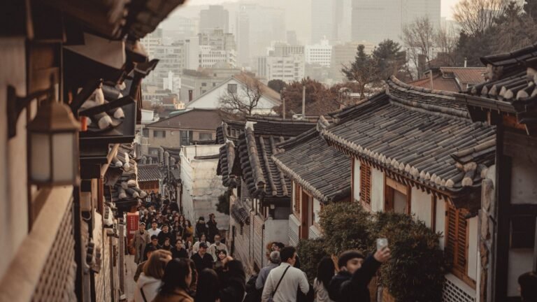 Traditional tiled roofs of Bukchon Hanok Village with modern Seoul skyscrapers in the background.