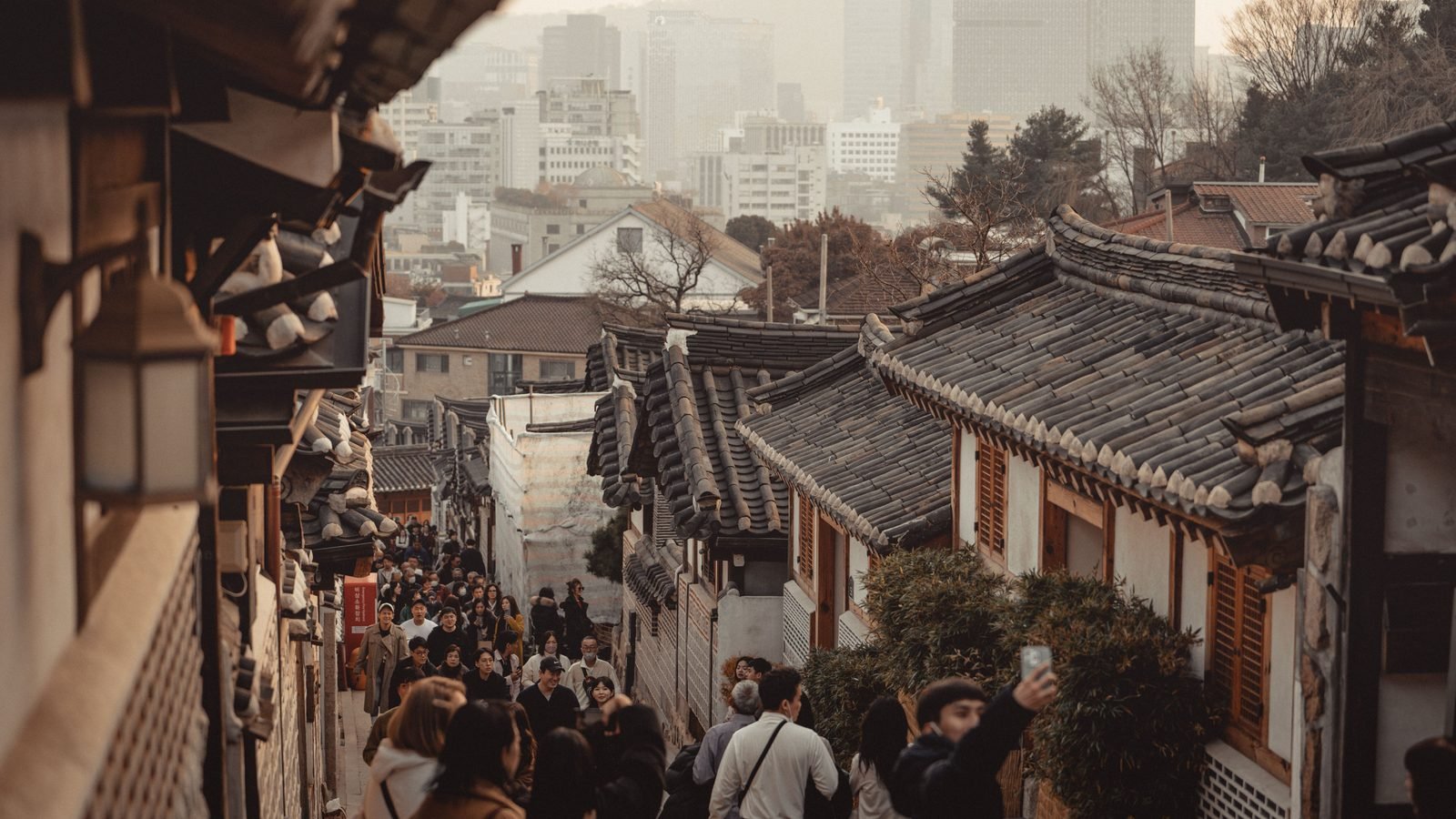 Traditional tiled roofs of Bukchon Hanok Village with modern Seoul skyscrapers in the background.