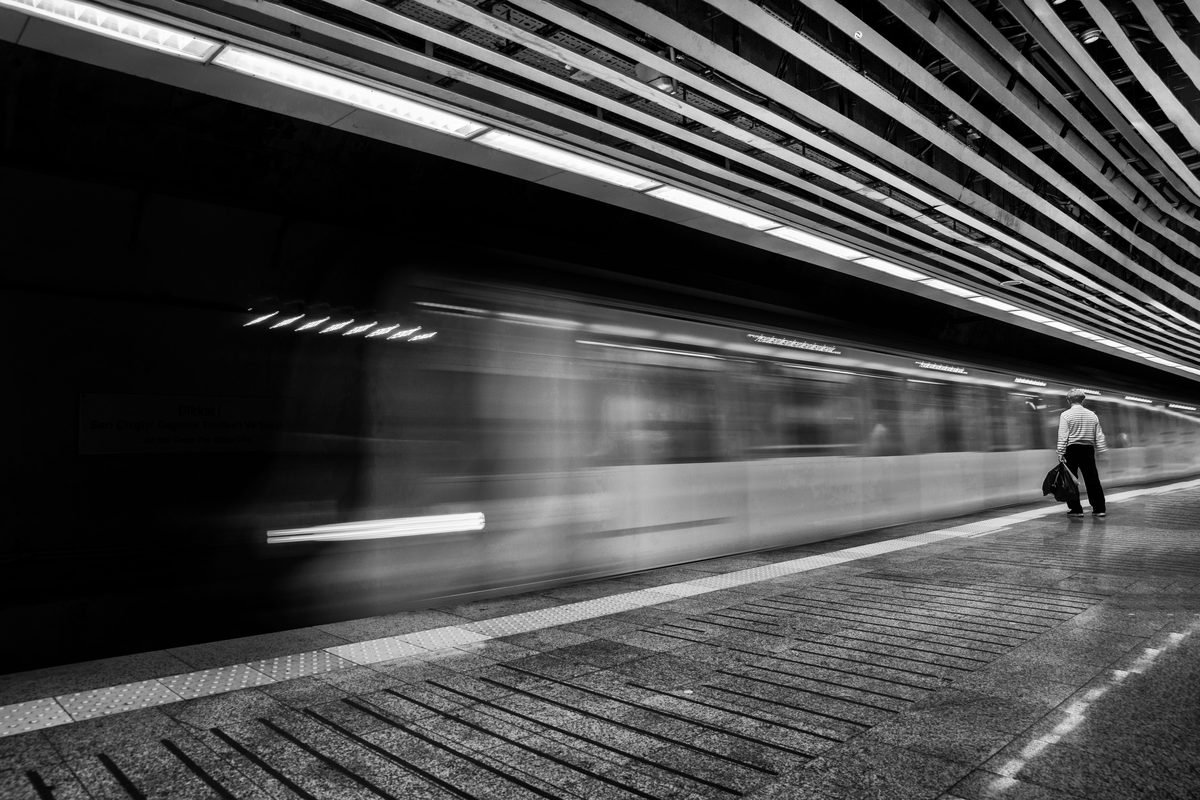 Motion blur of a speeding subway train on a platform with a solitary passenger.