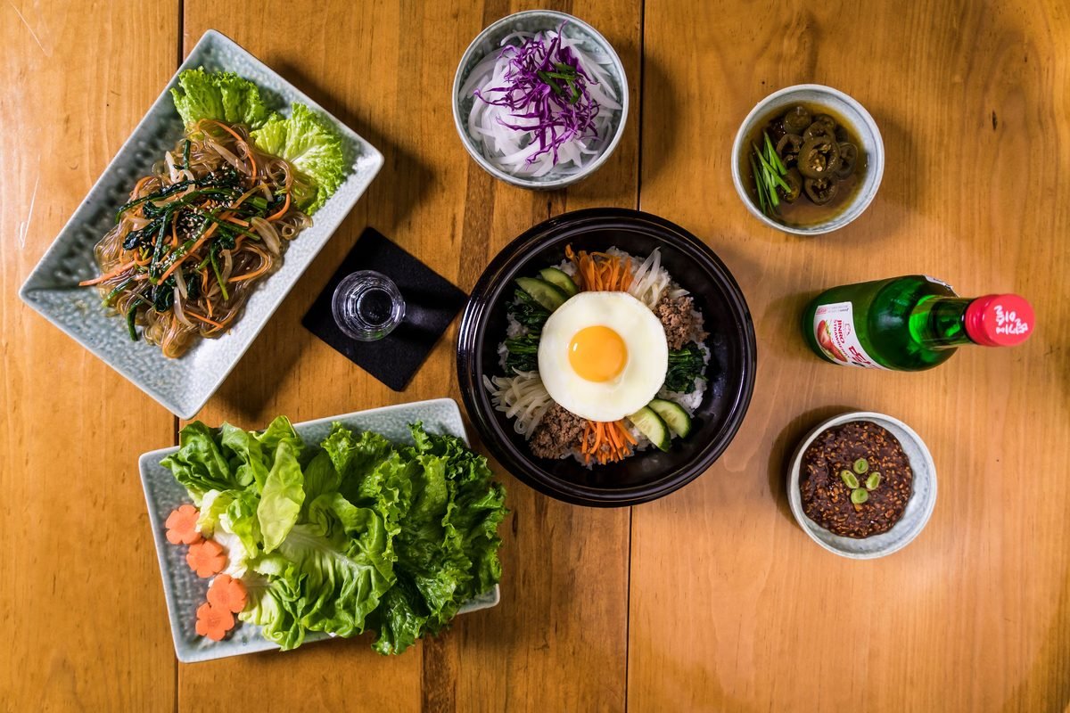 Overhead view of assorted Korean dishes including bibimbap and side dishes.