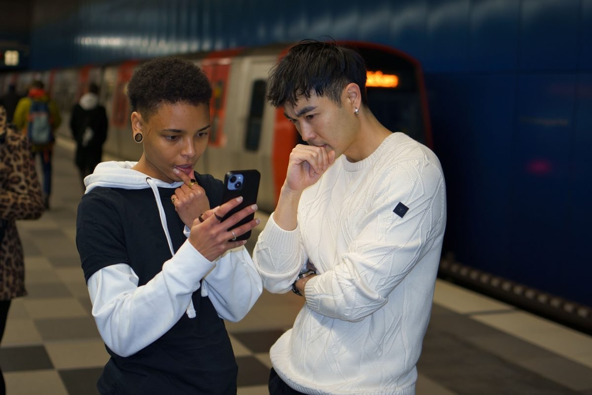 Friends interacting while looking at a smartphone in a subway station.