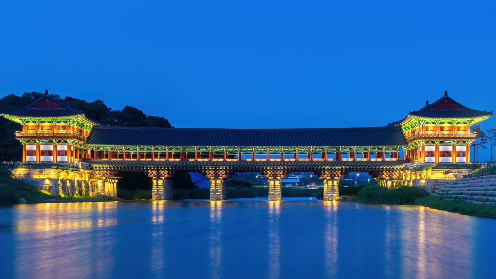 Illuminated Woljeonggyo wooden bridge reflected in river water at blue hour in Gyeongju South Korea