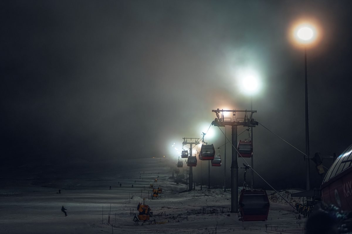 Ski lift illuminated at night amid fog and snow at a mountain resort