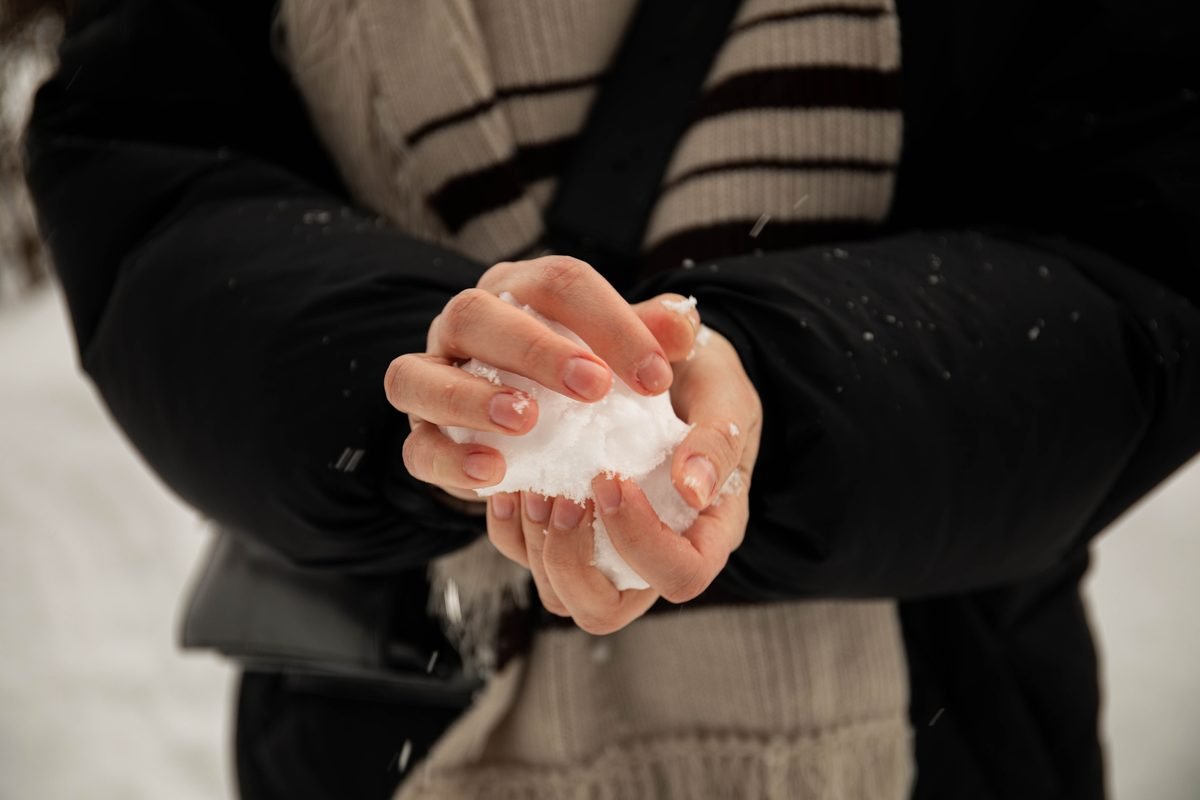 Close-up of hands wearing winter clothing holding a snowball outdoors.