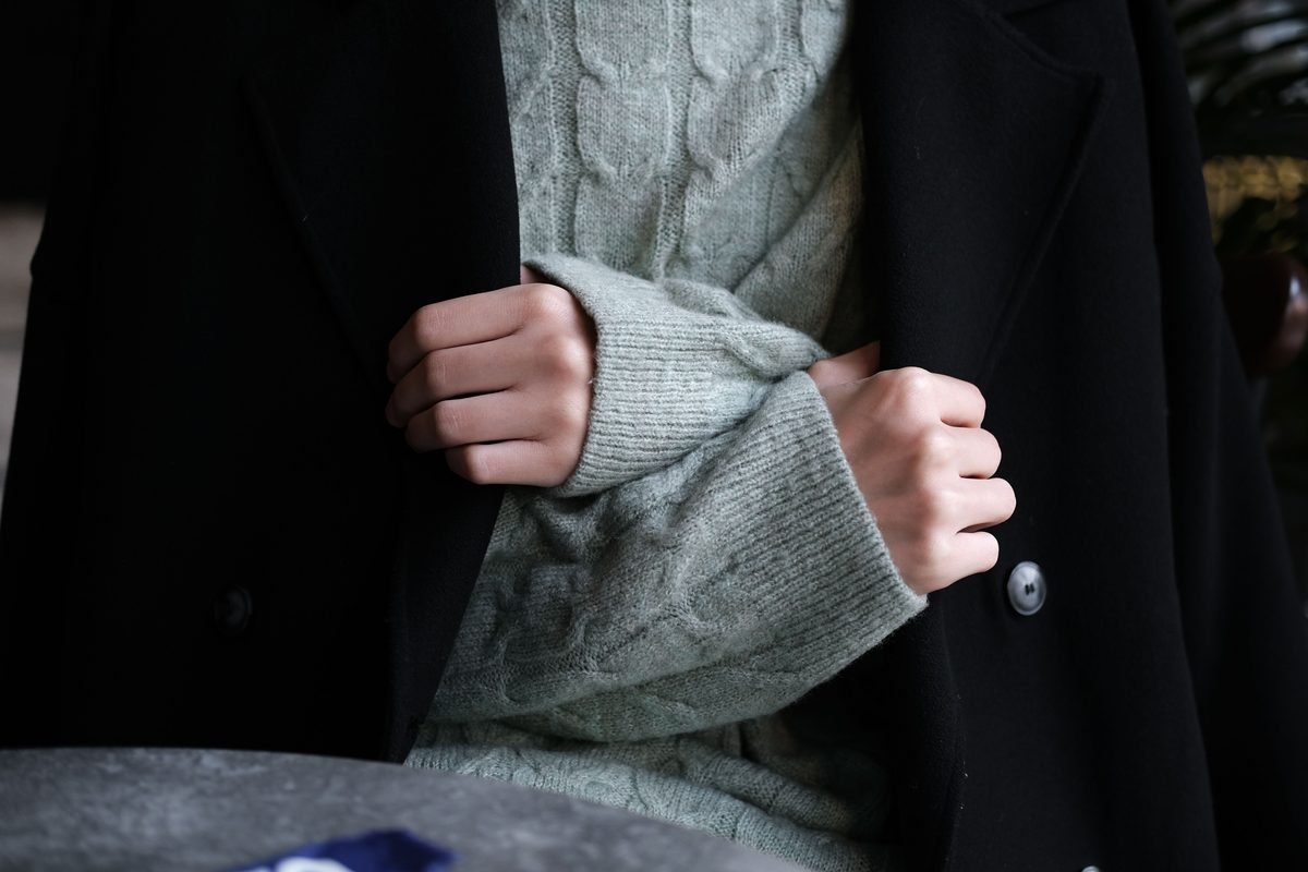 Close-up of hands wearing a knitted sweater under a heavy winter coat.