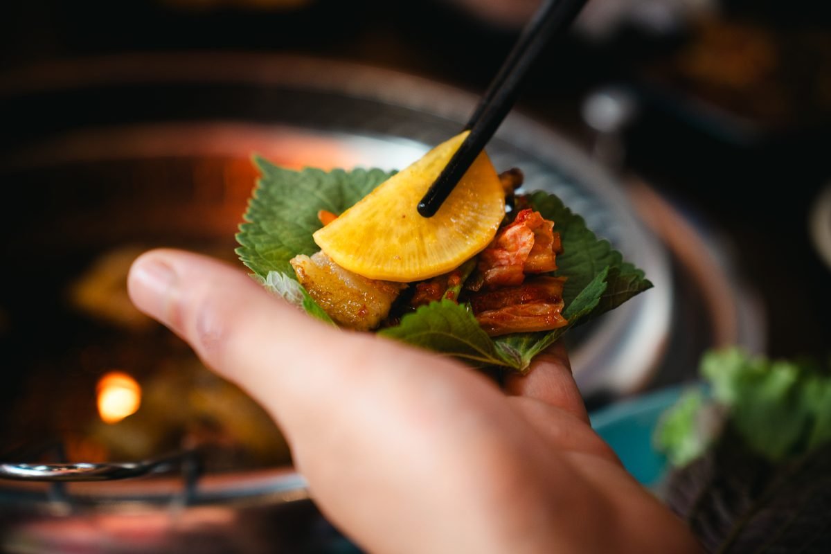 Korean BBQ leaf wrap showcasing daikon, kimchi, and pork belly