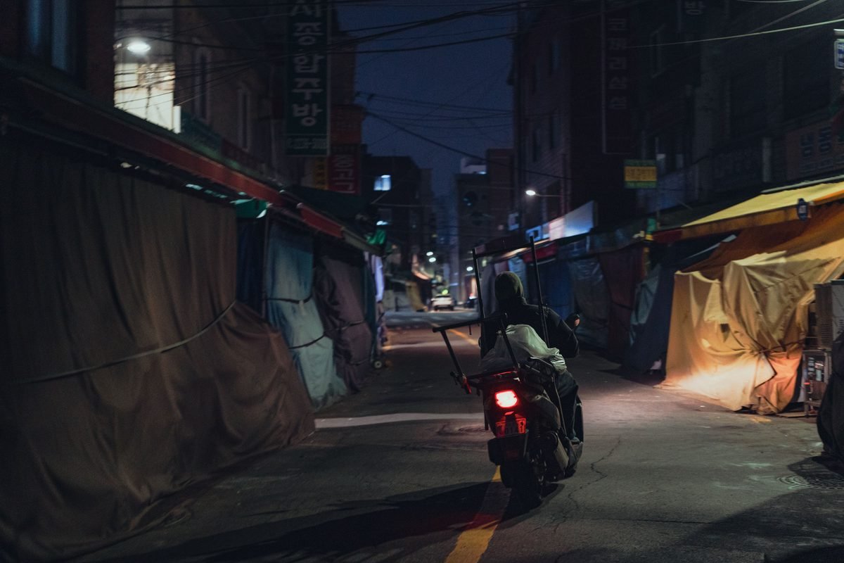 Moody night-time view of a motorcyclist navigating through Seoul alleyways