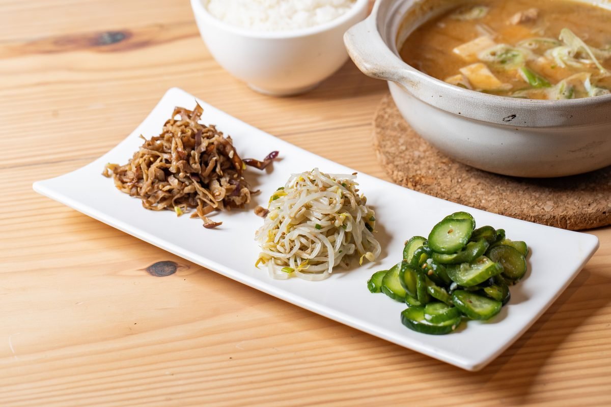 Spread of Korean side dishes with rice and vegetable soup on a wooden table