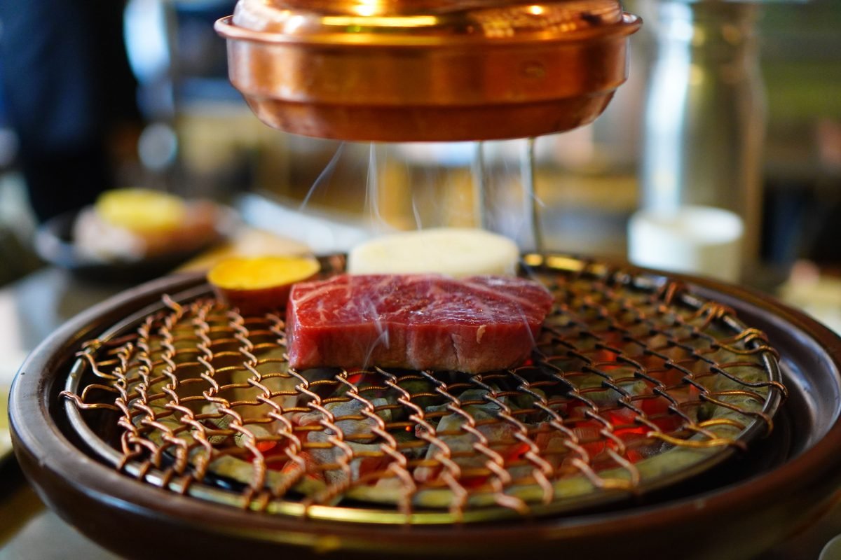 Close-up of raw beef on a Korean BBQ grill sizzling under a copper hood