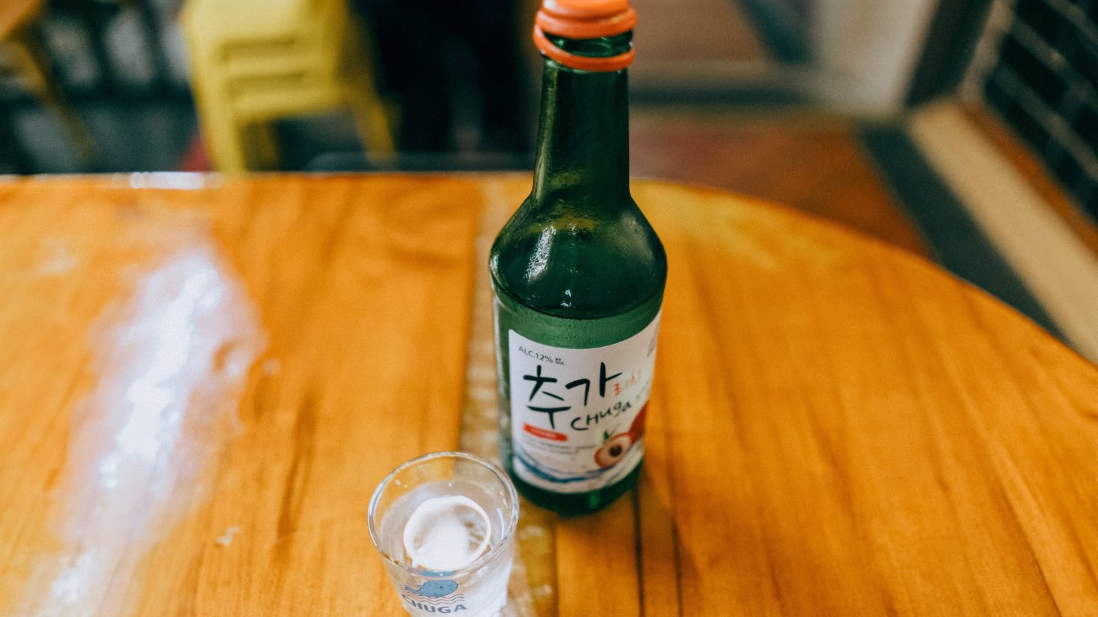 Green soju bottle and a small shot glass on a wooden table.