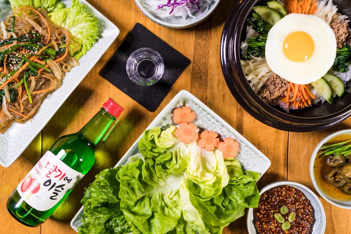 Flat lay of Korean dishes and a green soju bottle with a shot glass.