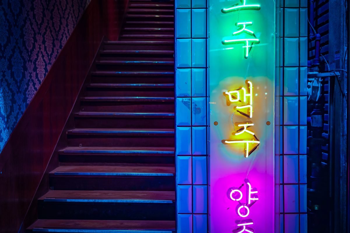 Colorful Korean neon signs lit up in a stairwell at night.