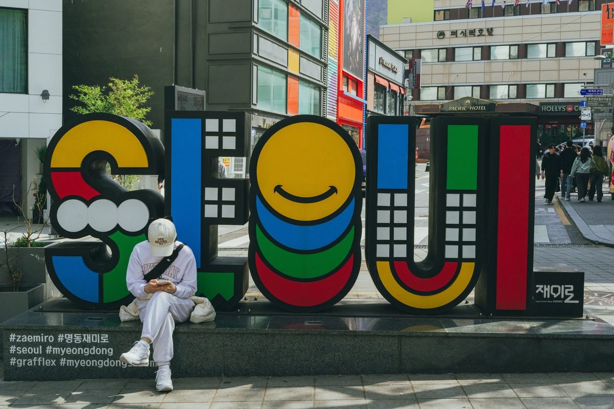 A person sitting near a colorful Seoul sign during daytime.