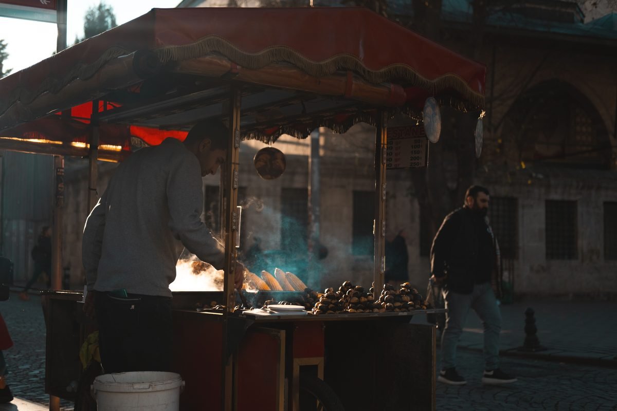 A street vendor cooks corn on a cart with steam rising at night