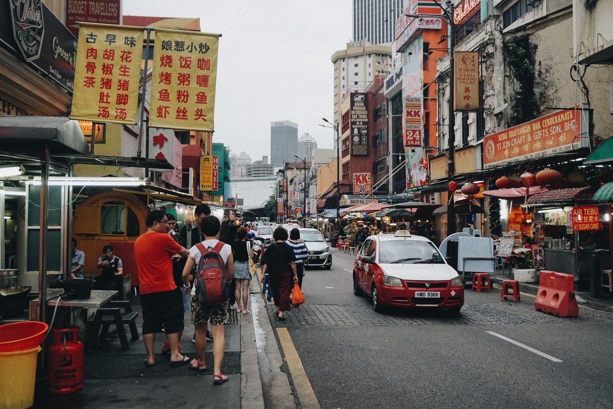 Busy street in Kuala Lumpur lined with shops, Chinese signs, and a red and white taxi