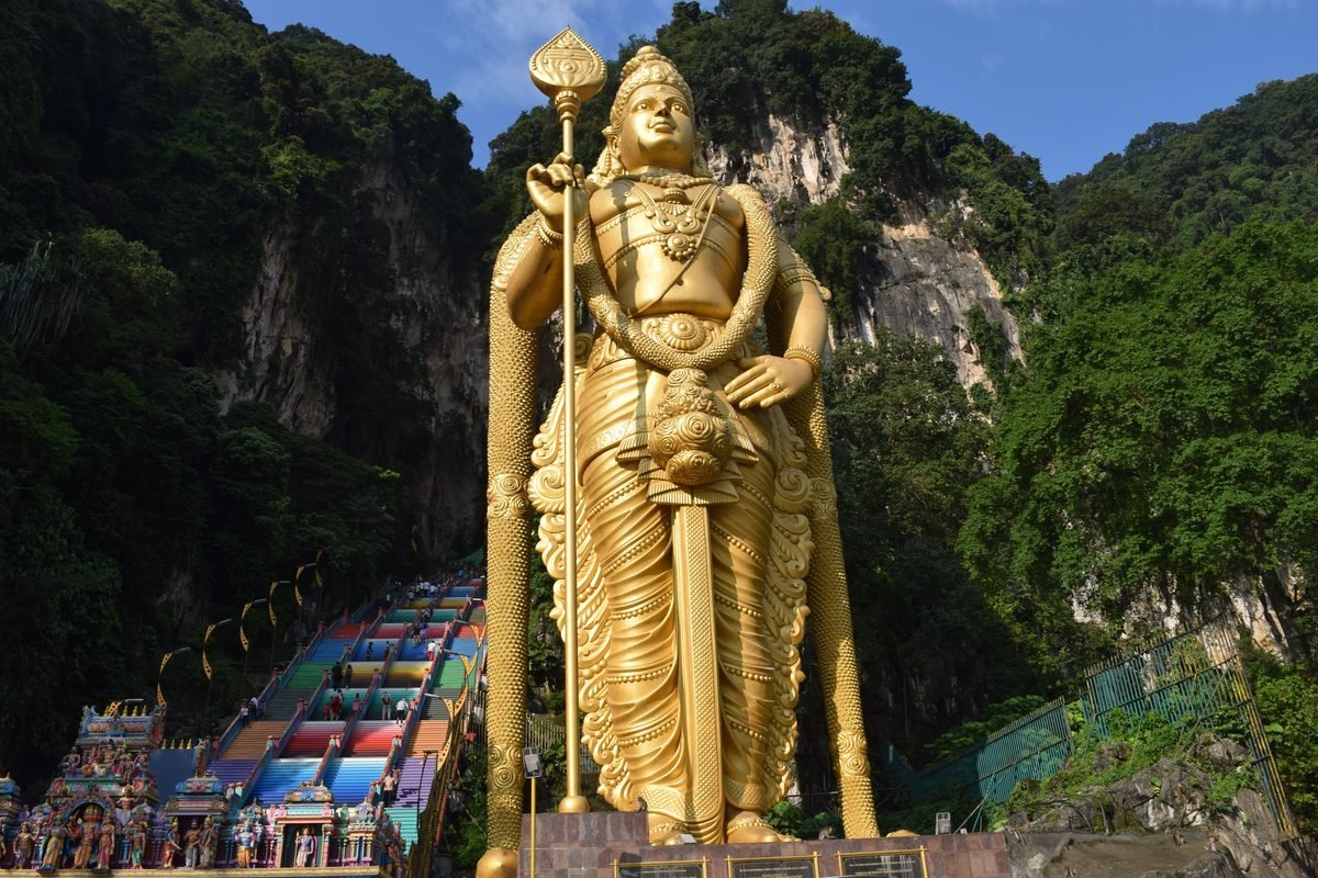 Majestic golden Lord Murugan statue at Batu Caves against a forested cliff