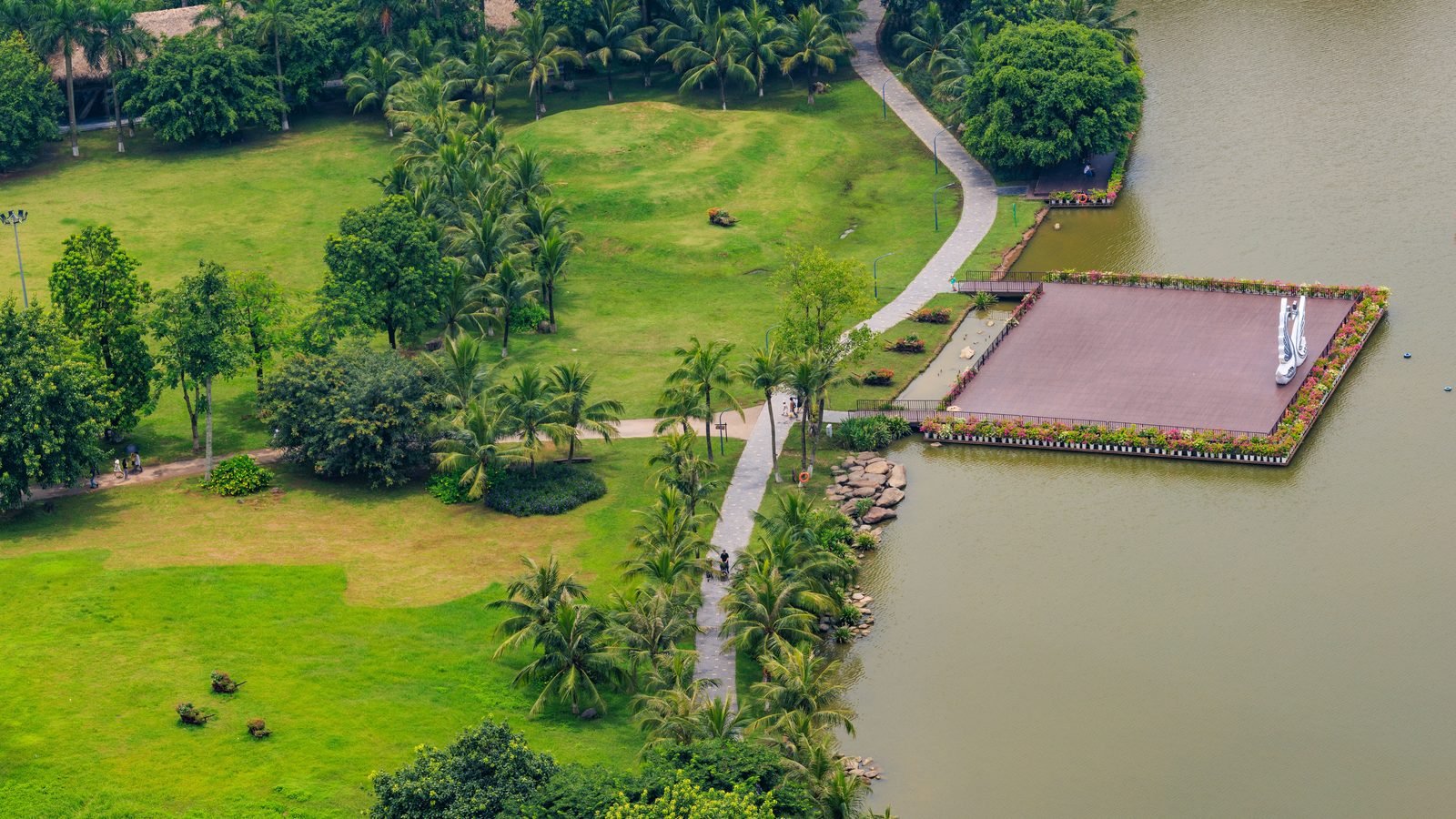 Aerial view of a lush green urban park with a winding pathway and lake