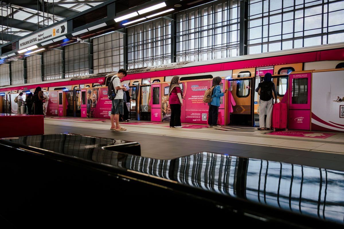 Commuters waiting on a modern pink and yellow metro station platform in Malaysia