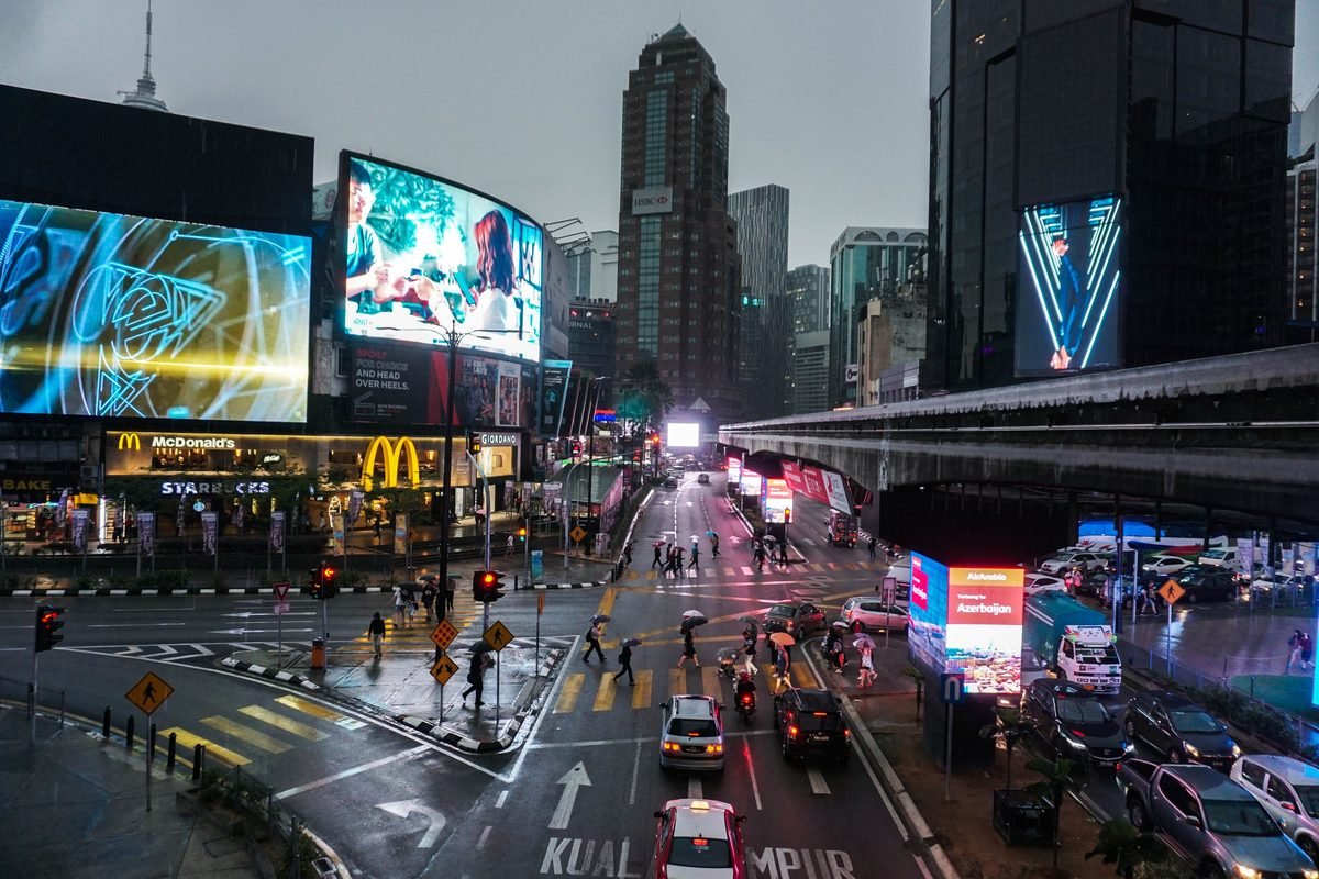 Busy illuminated street intersection with digital billboards and traffic in Kuala Lumpur