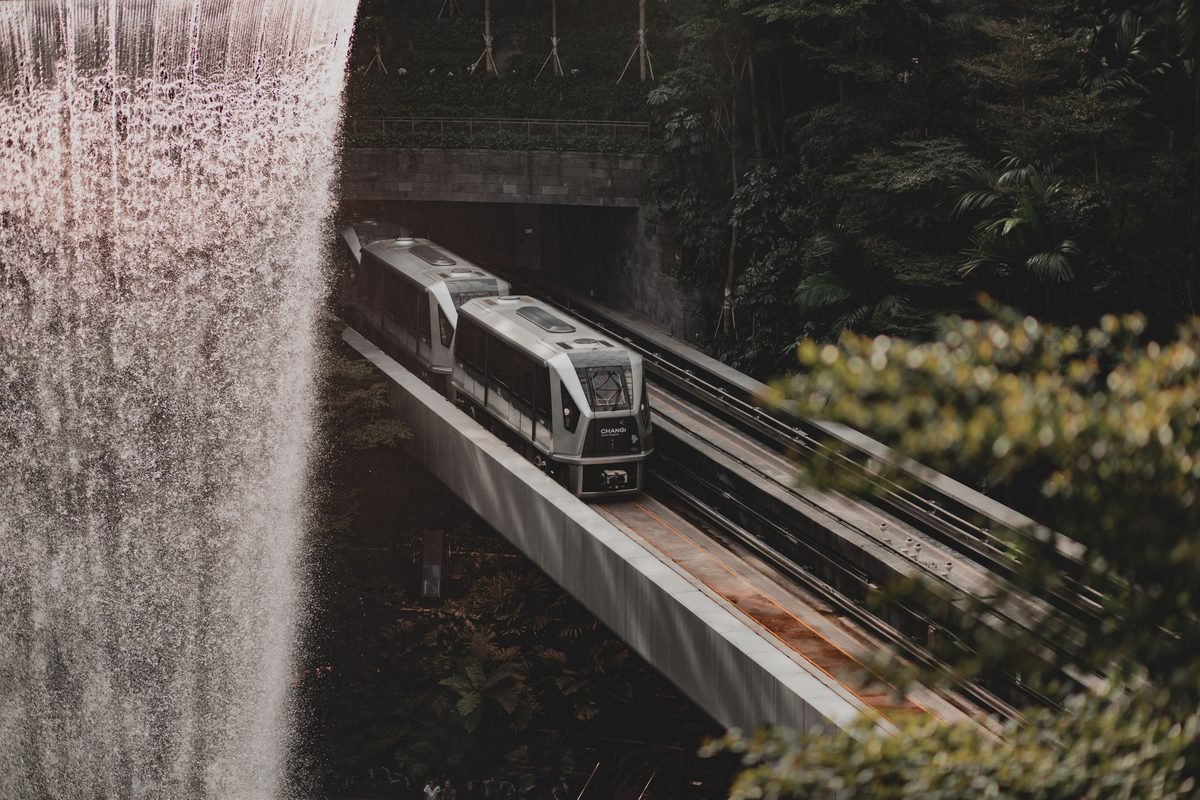 Modern train running along elevated tracks near a waterfall and lush forest
