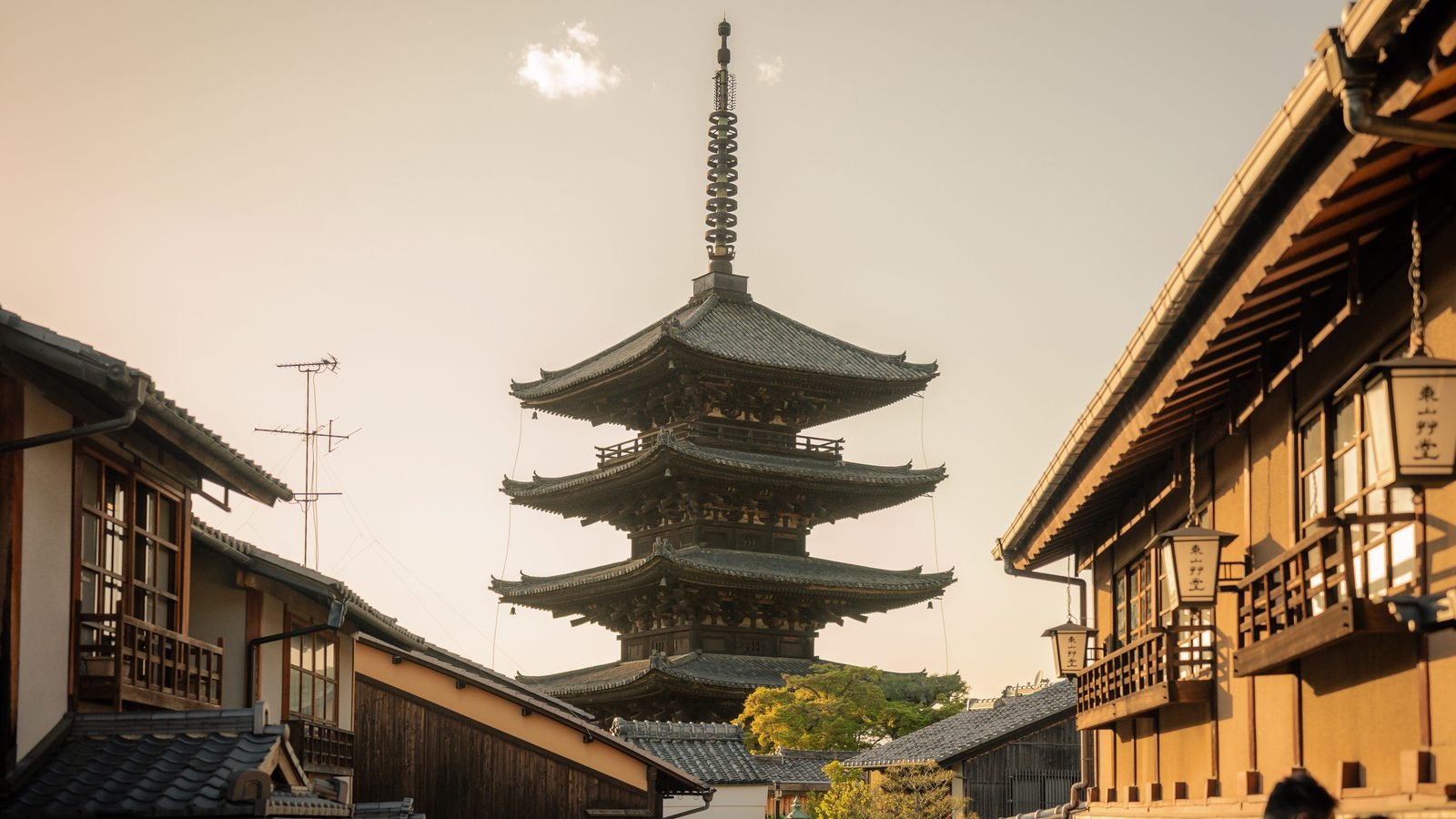 Traditional wooden Japanese Yasaka Pagoda towering over a historic street in Kyoto at sunset.