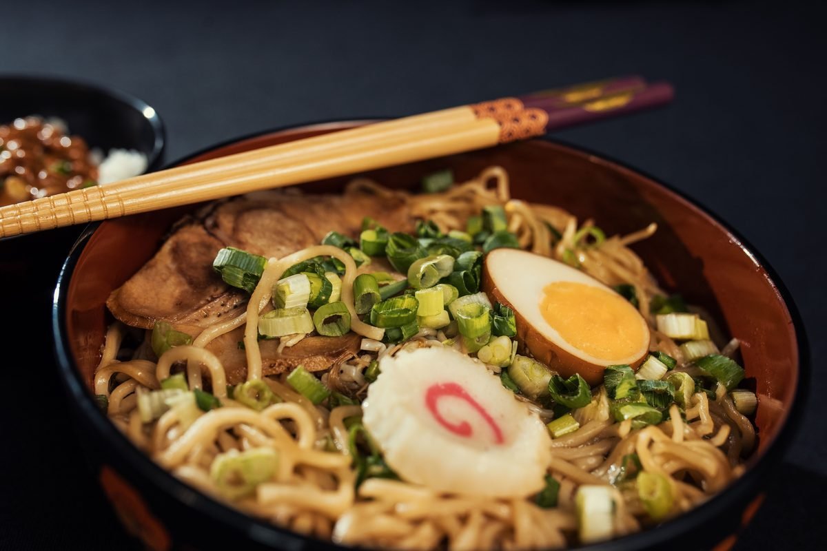 Bowl of traditional Japanese ramen with egg and scallions served with chopsticks.