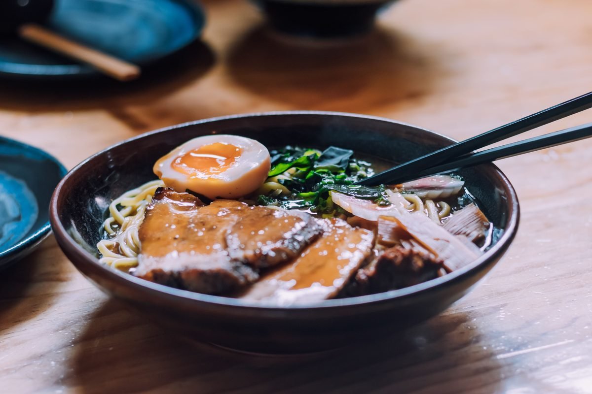 Close-up of a savory ramen bowl with pork, egg, and chopsticks on wooden table.