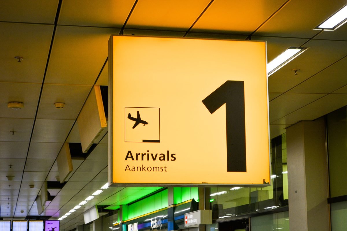 Bright yellow arrivals sign with an airplane symbol in an airport terminal.